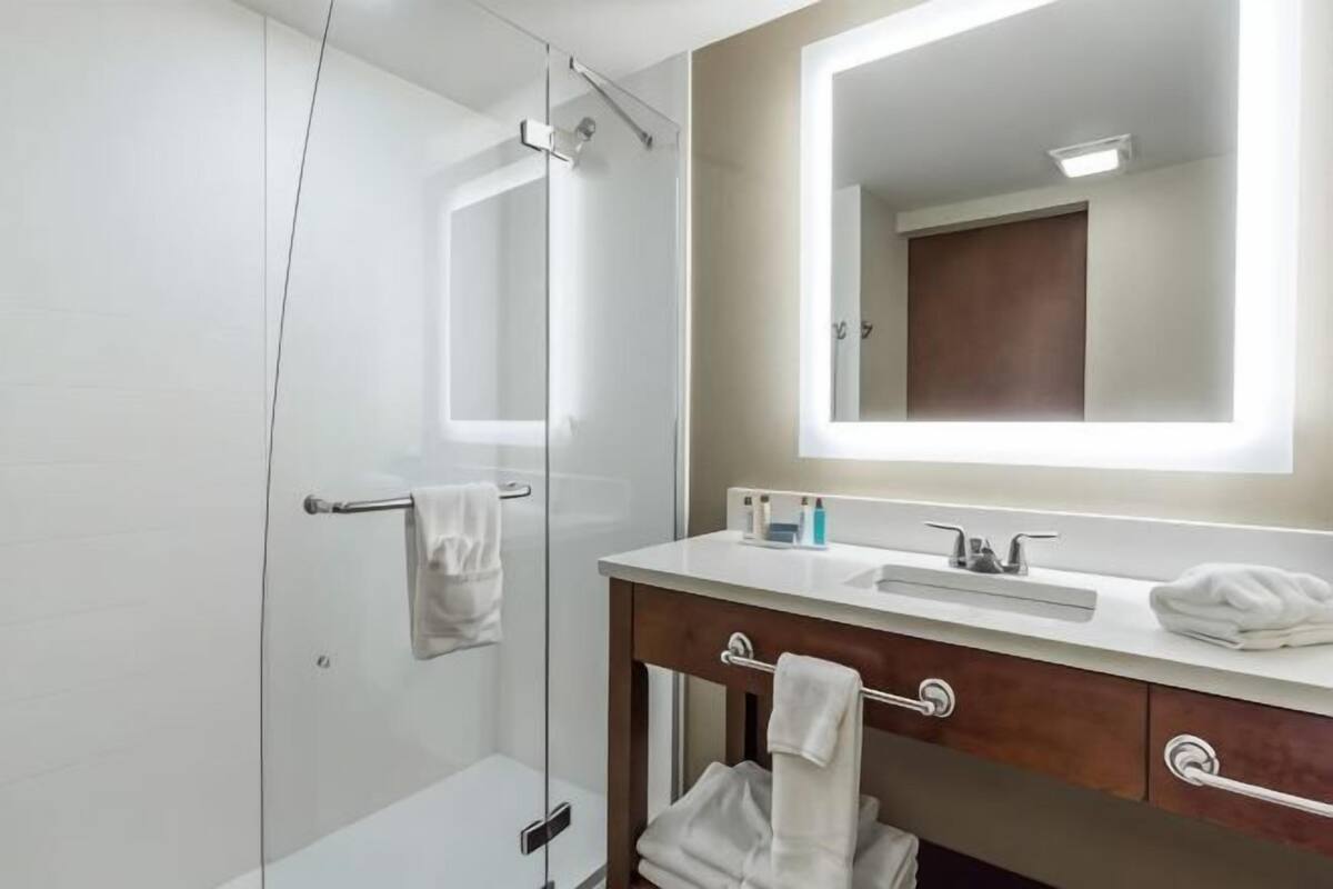 Een moderne badkamer met een glazen douchecabine, een wit wastafelmeubel, een grote spiegel en houten kastjes.