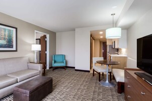 Habitación de hotel con sofá, sillón, televisión y una pequeña mesa de comedor.
