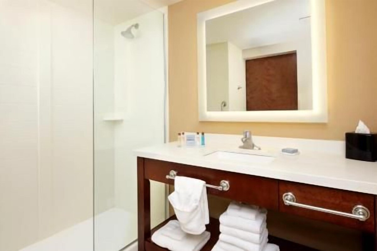Une salle de bain avec une douche à parois de verre, un lavabo blanc avec un miroir au-dessus, et un meuble-lavabo en bois avec des serviettes.