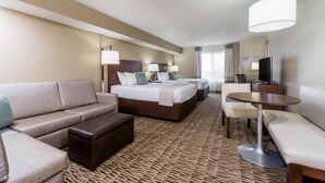 Habitación de hotel con cama, dos mesitas de noche, sofá, una mesita pequeña y televisor.