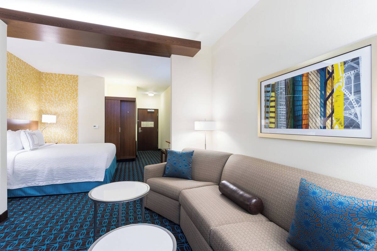 Una habitación de hotel con una cama, un sofá, una mesita y un cuadro en la pared.