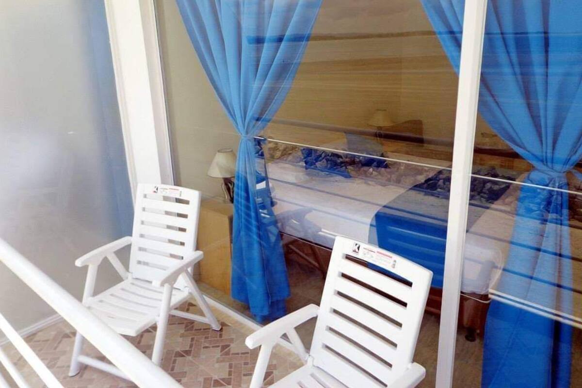 A room with a bed covered by a blue canopy, two white chairs, and a lamp on a table.