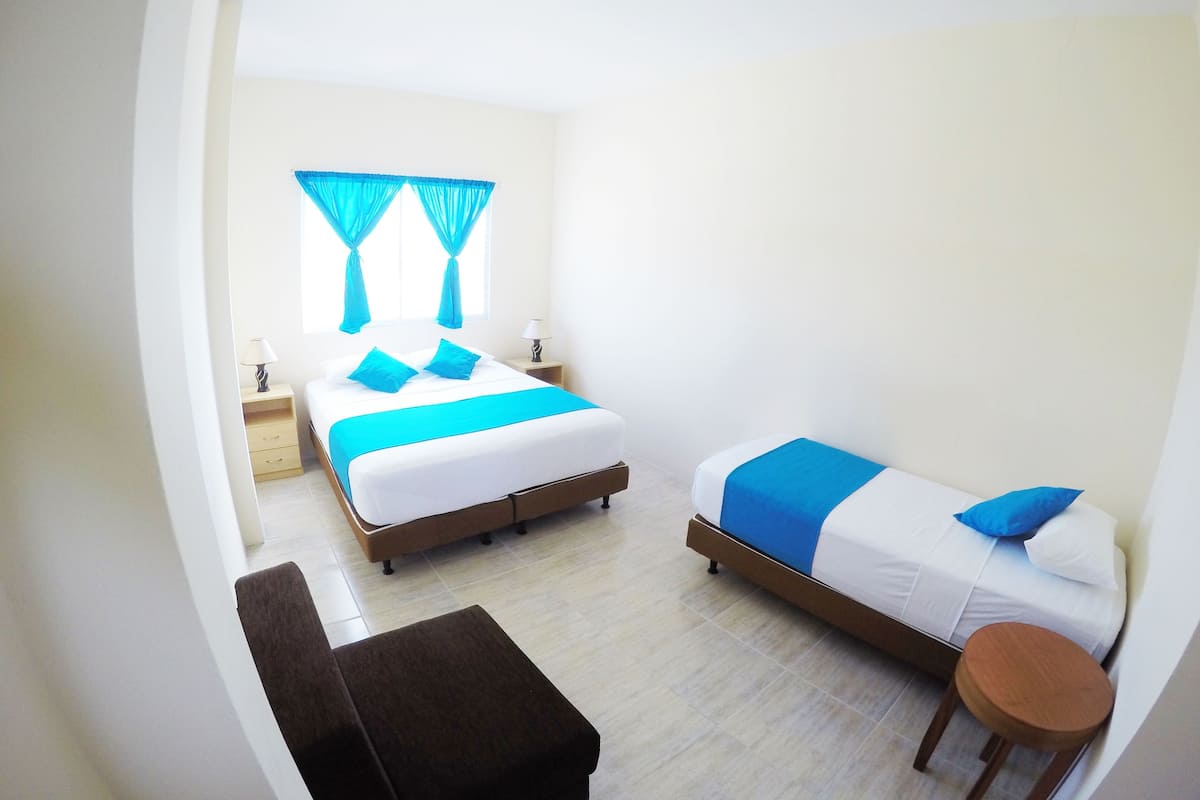 A hotel room with two beds, a small table, and a bench.
