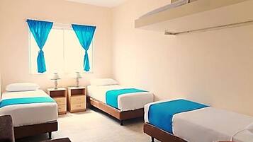 A hotel room with three single beds, a desk, and a chair. There are two bedside tables with lamps.