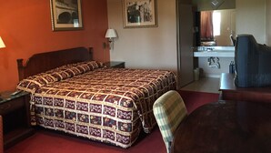 Et hotelværelse med en stor seng, et skrivebord, en stol, en ventilator i loftet samt et badeværelse med håndvask og spejl.