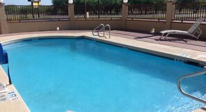Ein rechteckiger Pool mit einer Metallleiter, umgeben von einer gefliesten Terrasse und einem Metallzaun.