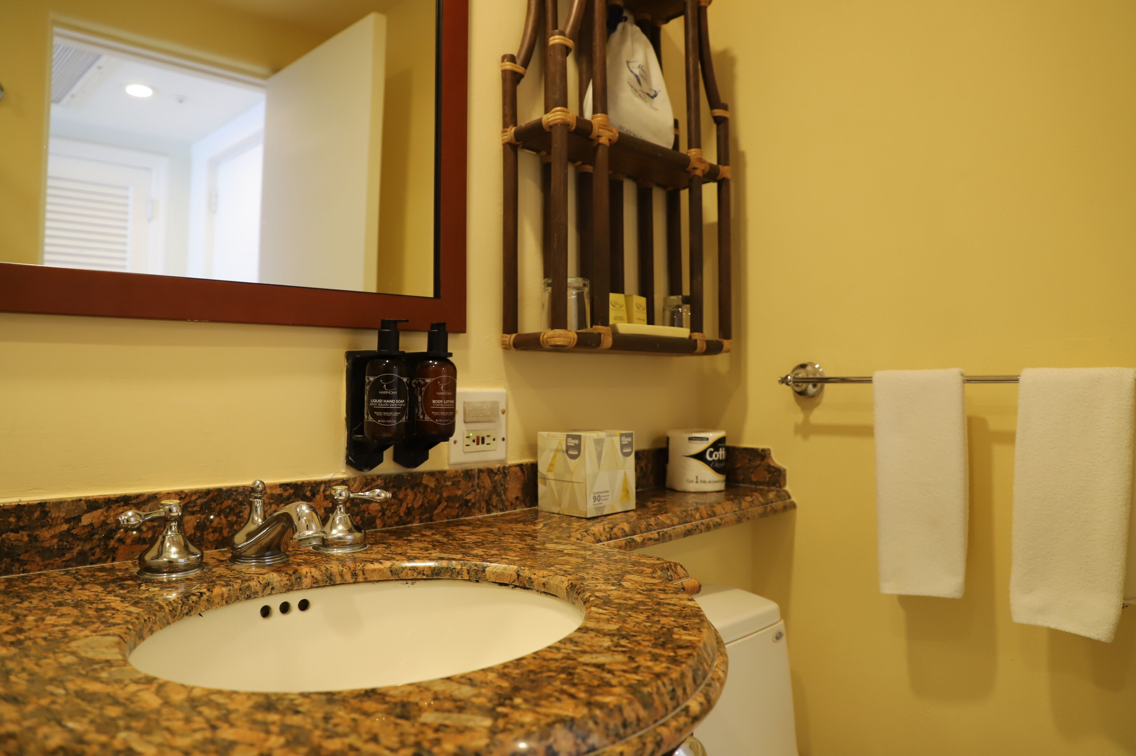 A bathroom with a granite countertop sink, a mirror, a towel rack, and toiletries.