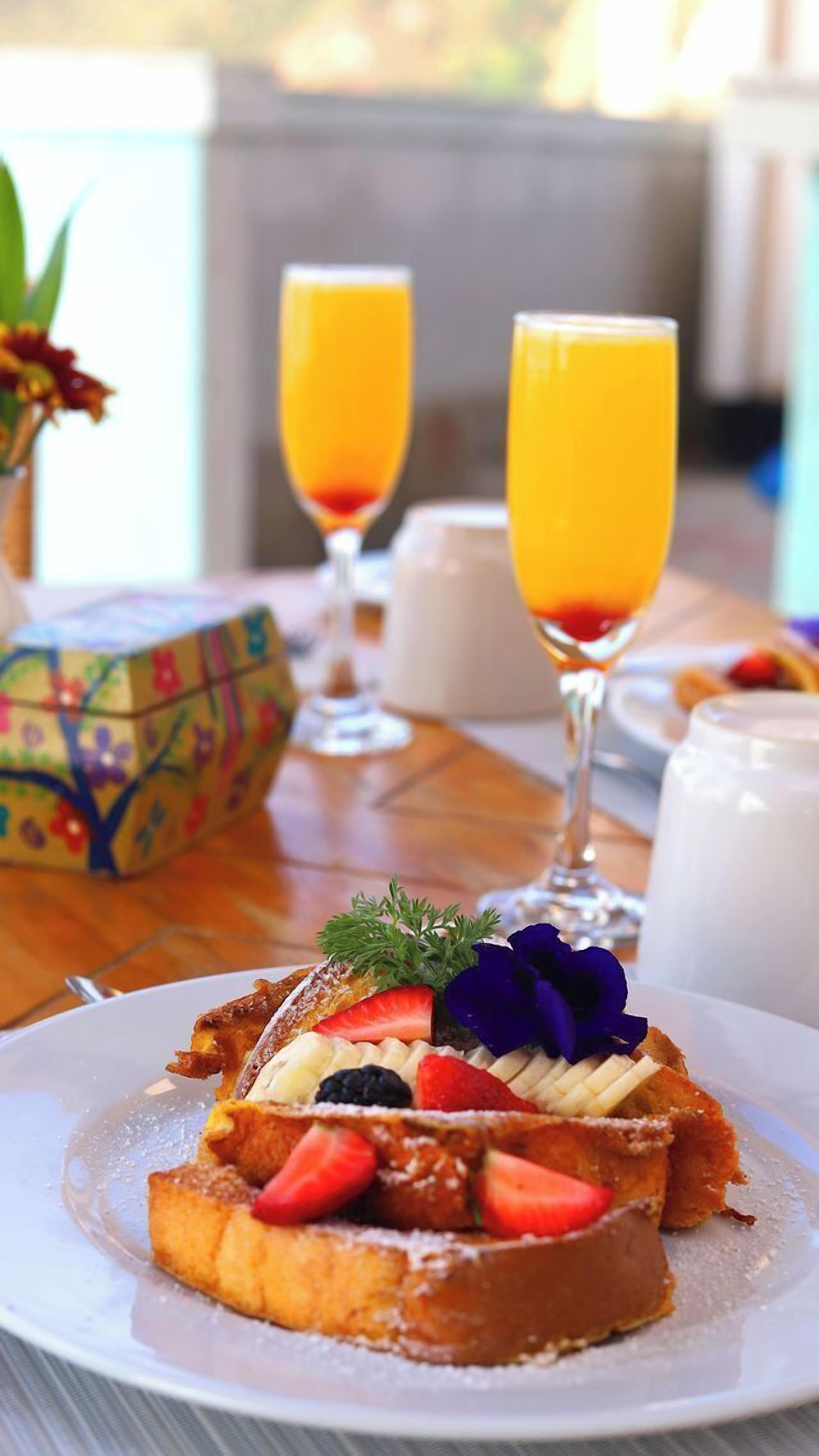 Een ontbijttafel met een bord Franse toast, belegd met fruit, en een glas sinaasappelsap.