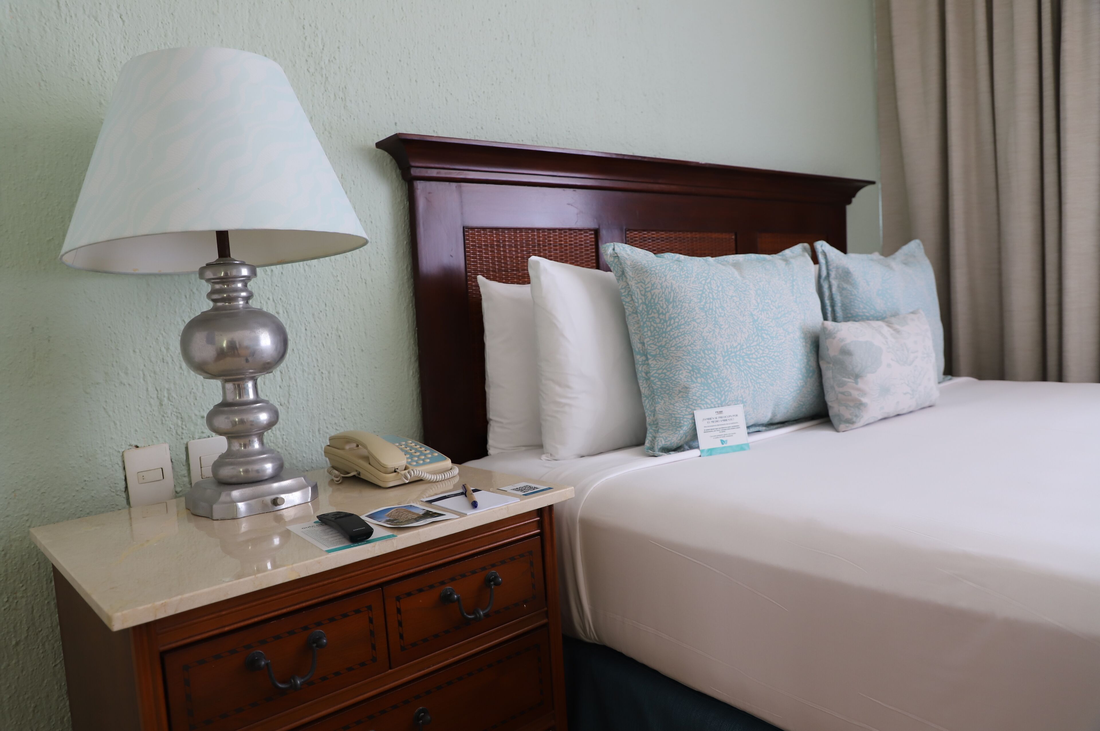 A hotel room with a bed, a nightstand, a lamp, a telephone, and a few pillows.