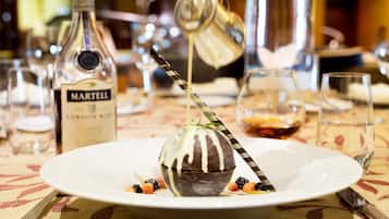 Un postre sobre un plato blanco con una cuchara a rayas, rodeado de varias botellas y vasos sobre un mantel.