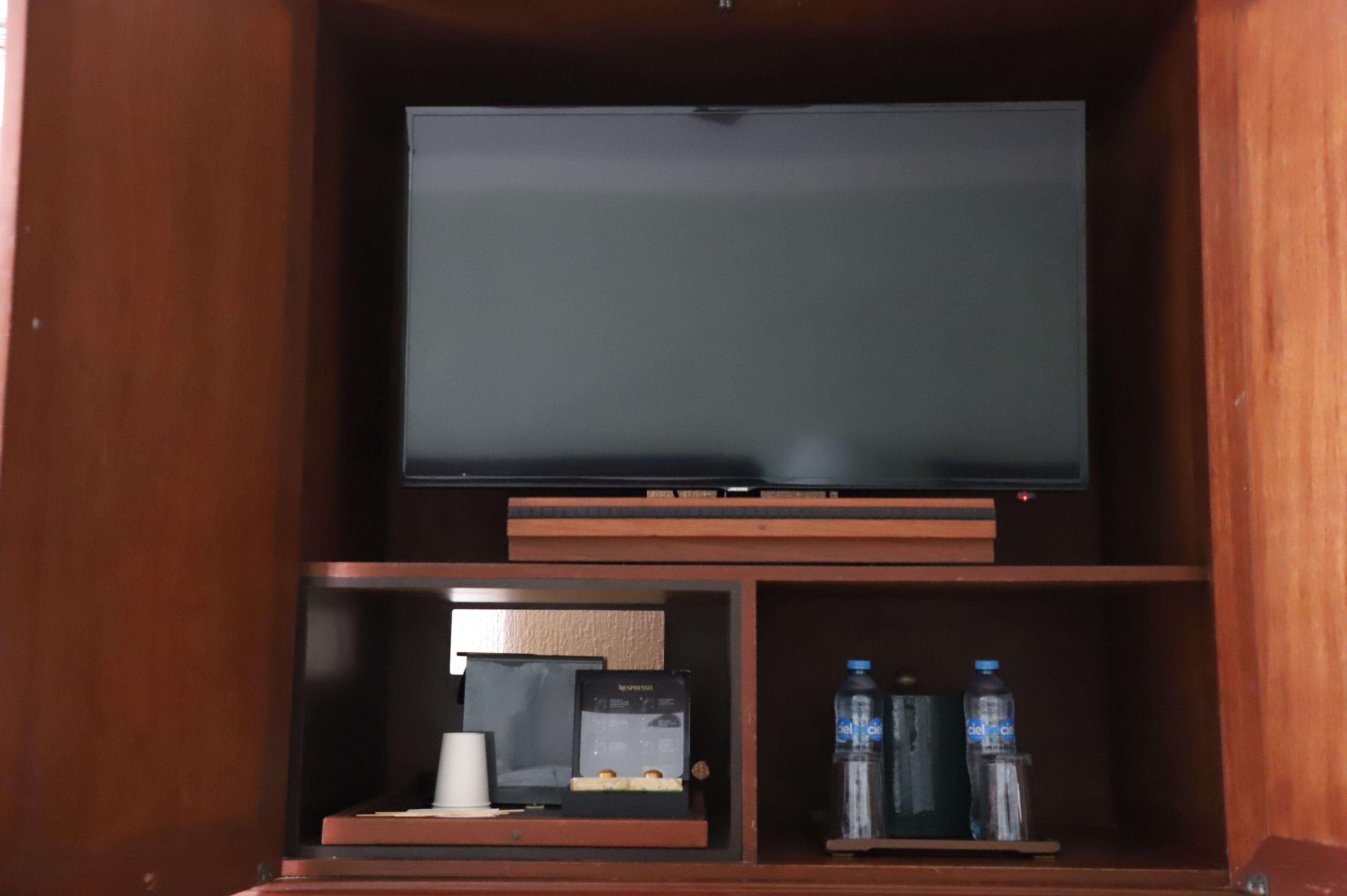 Ein Fernseher auf einem Holzboden, darunter ein Kaffeeautomaten und Wasserflaschen.