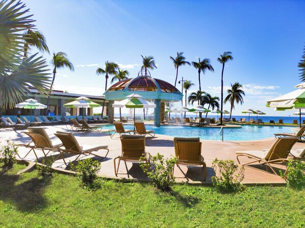 A pool area with lounge chairs and umbrellas, surrounded by palm trees and a clear view of the ocean. - Pierre Mundo Imperial (Acapulco)