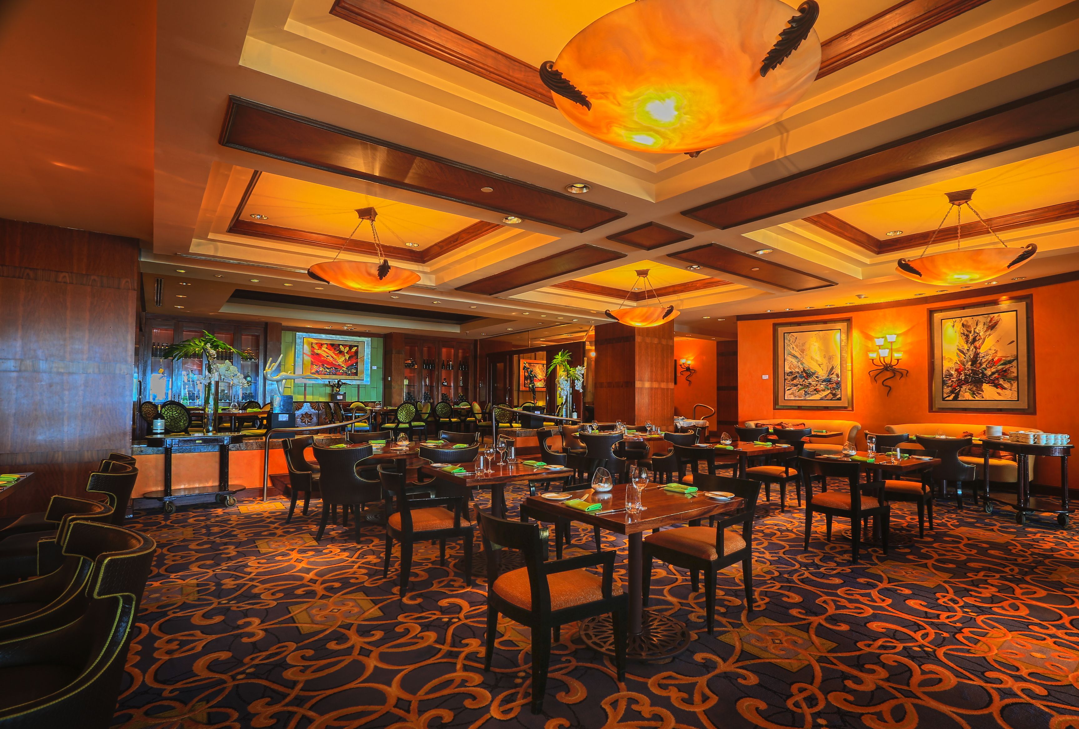 Un restaurant doté d’un tapis à motifs, de meubles en bois et de luminaires suspendus.
