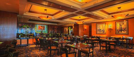 A restaurant with a patterned carpet, wooden furniture, and hanging pendant lights.