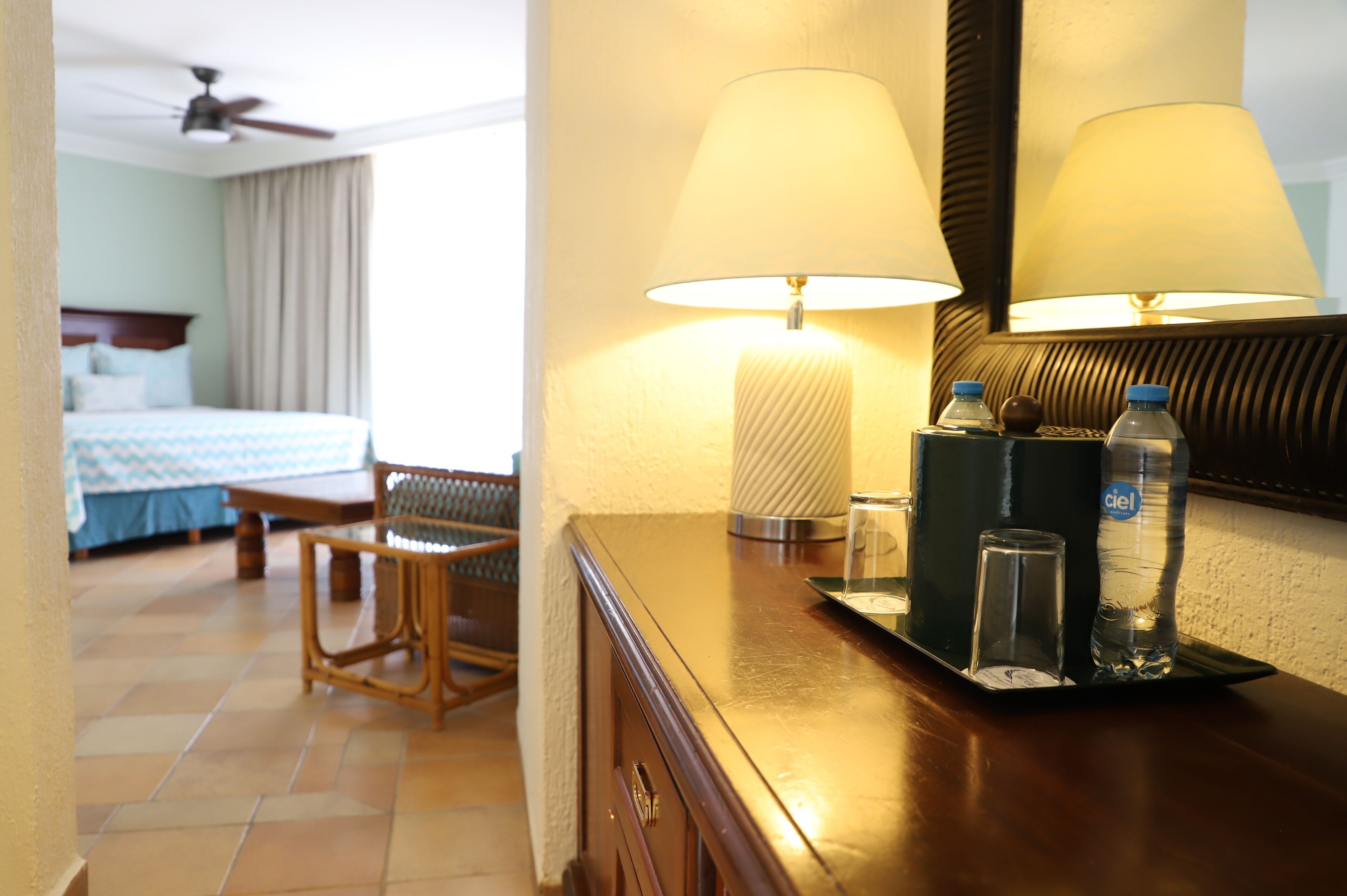 A hotel room with a bed, a desk, a chair, a lamp, and a mirror.