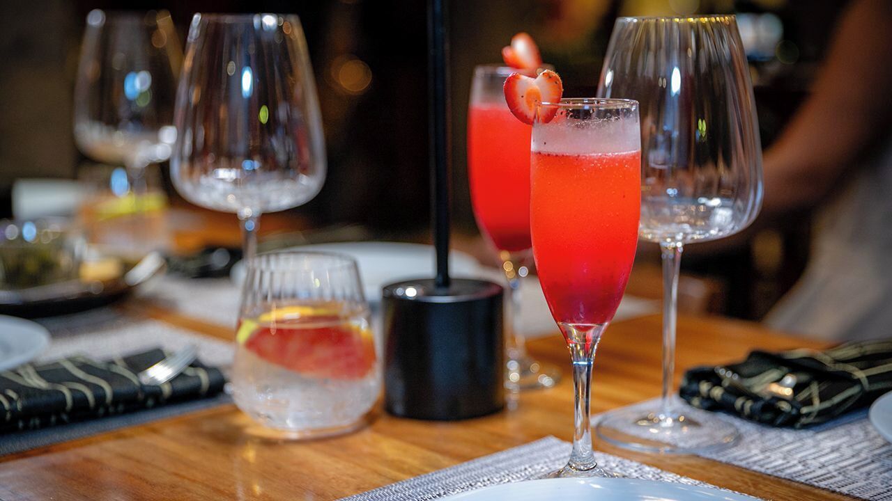 Un bar con varios vasos de bebidas rojas, un shaker de cócteles y una botella de agua.