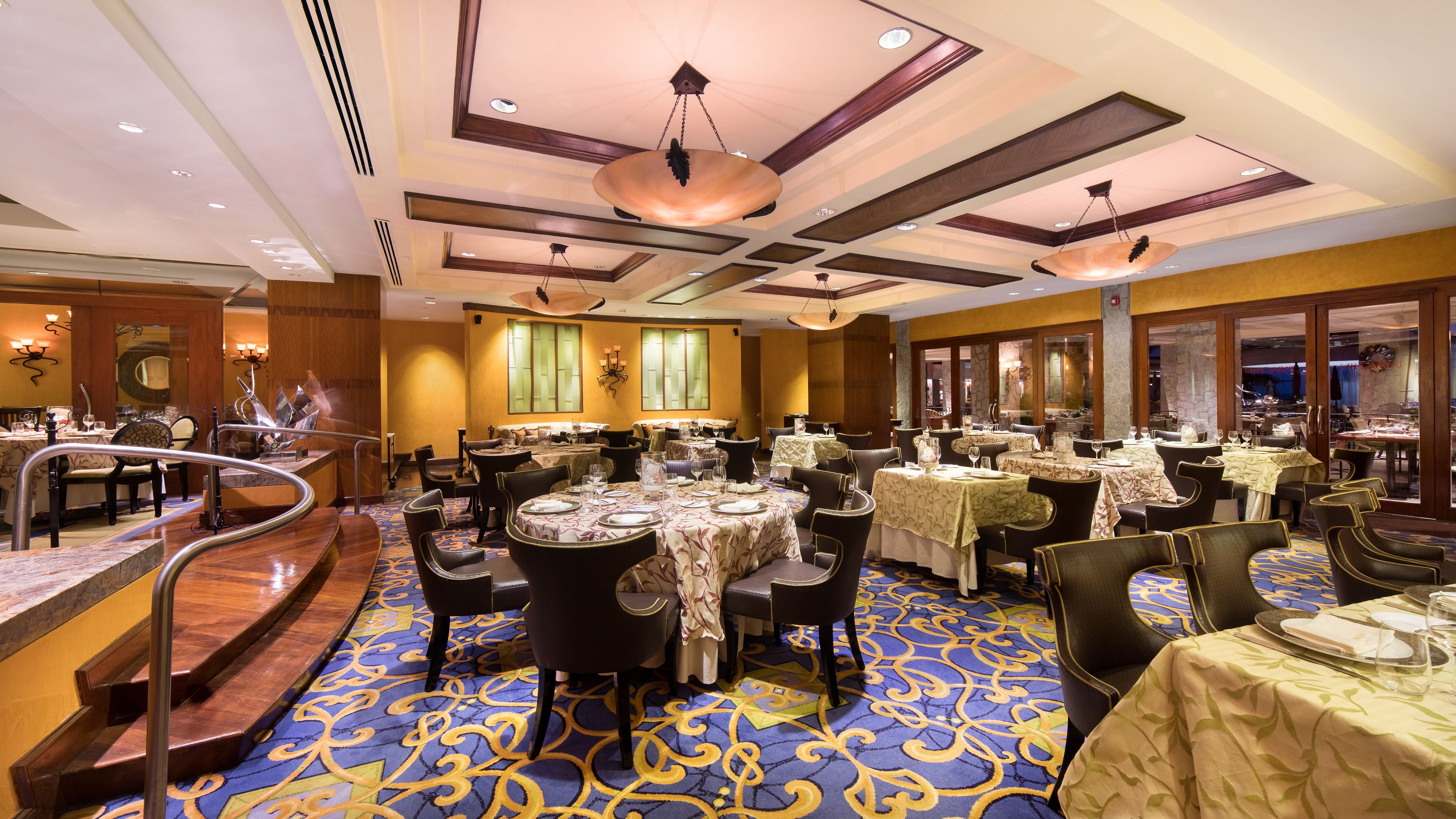Un comedor de hotel con varias mesas, sillas y una escalera central.