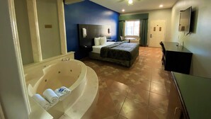 A hotel room with a large bathtub, a bed, a desk, and a television. - Texas Inn Alamo (Alamo)