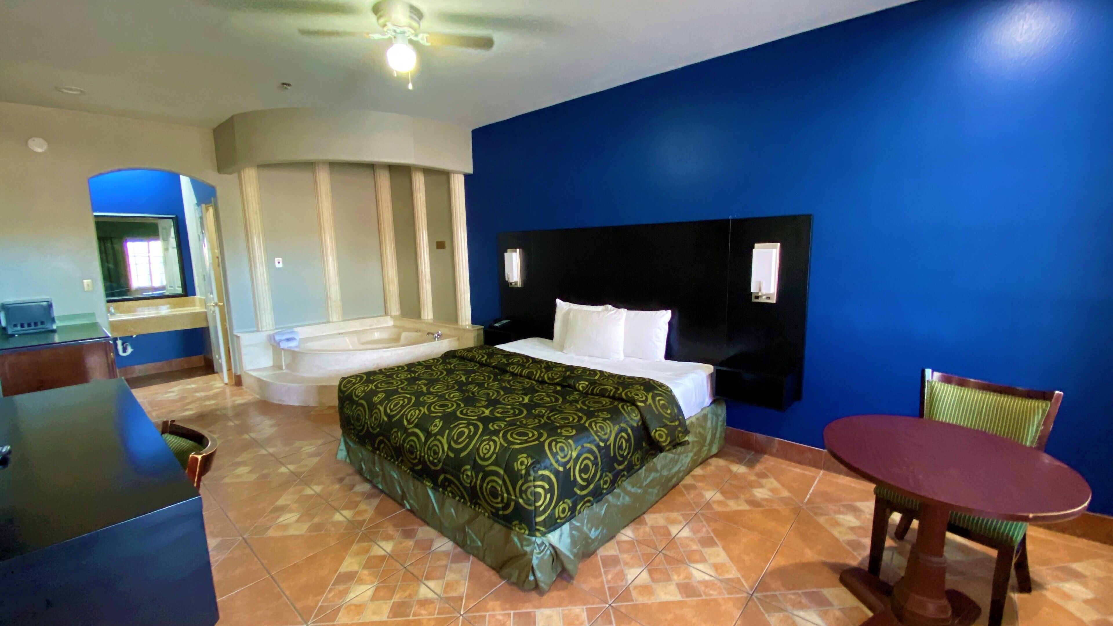 A hotel room with a bed, a small table, a chair, a desk, and a bathtub.