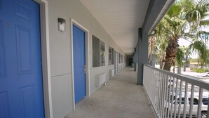 A corridor with blue doors, a white railing, and parked cars. - Texas Inn Alamo (Alamo)