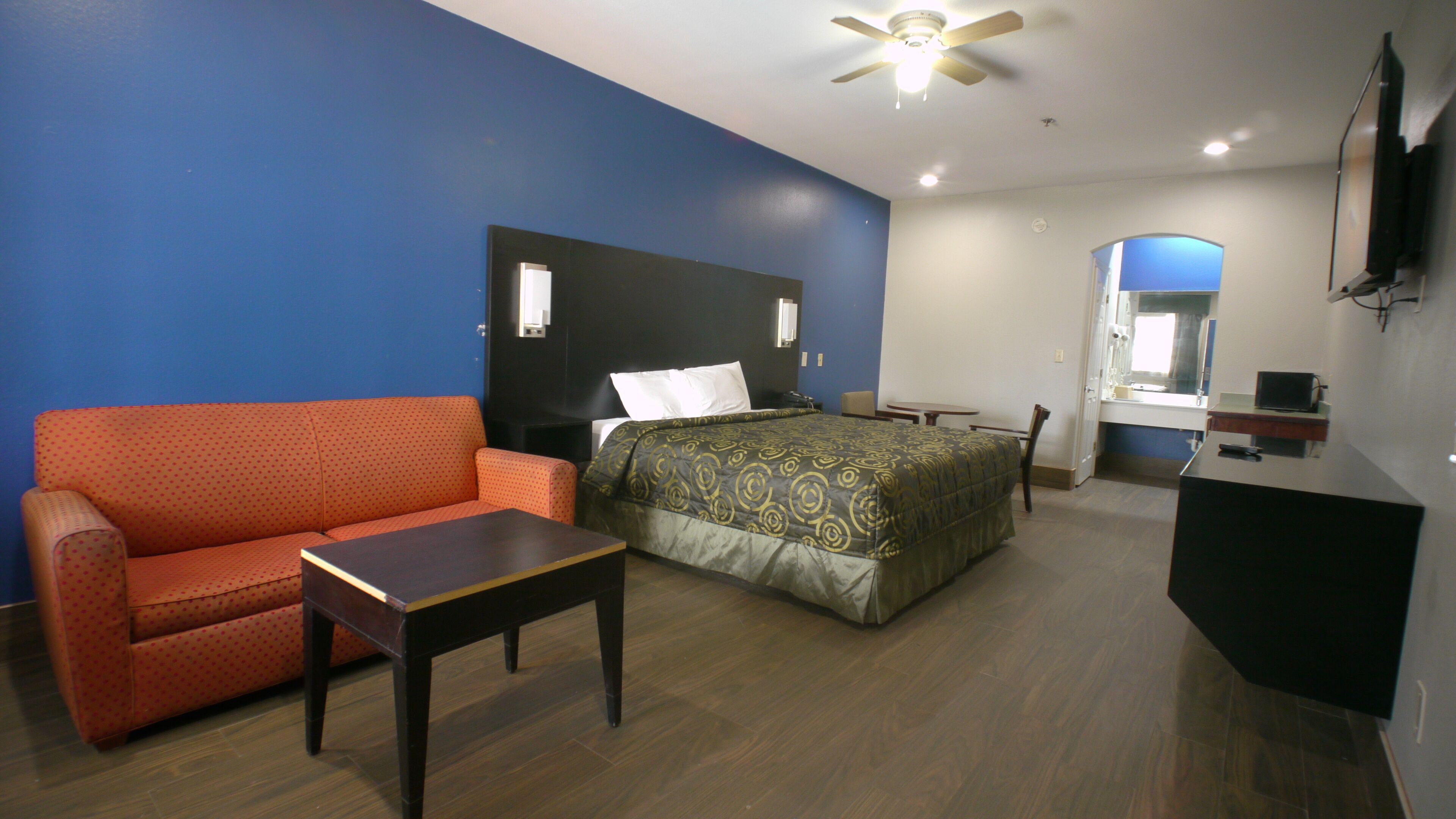 Una habitación de hotel con cama, sofá, escritorio, espejo y televisión.