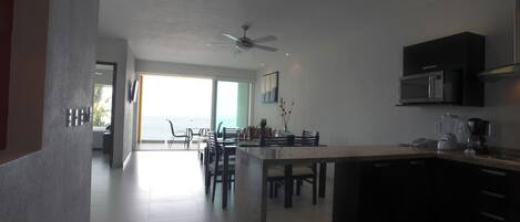 A modern kitchen with a dining area, large windows, and a ceiling fan.