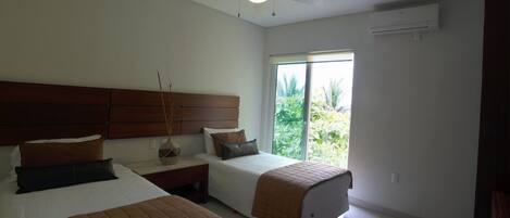 Un dormitorio con dos camas, un ventilador de techo y un ventanal con vistas a zonas verdes.