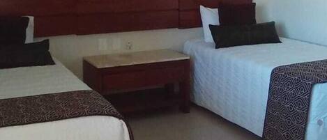 A room with two beds, a wooden headboard, a nightstand, and a ceiling fan.