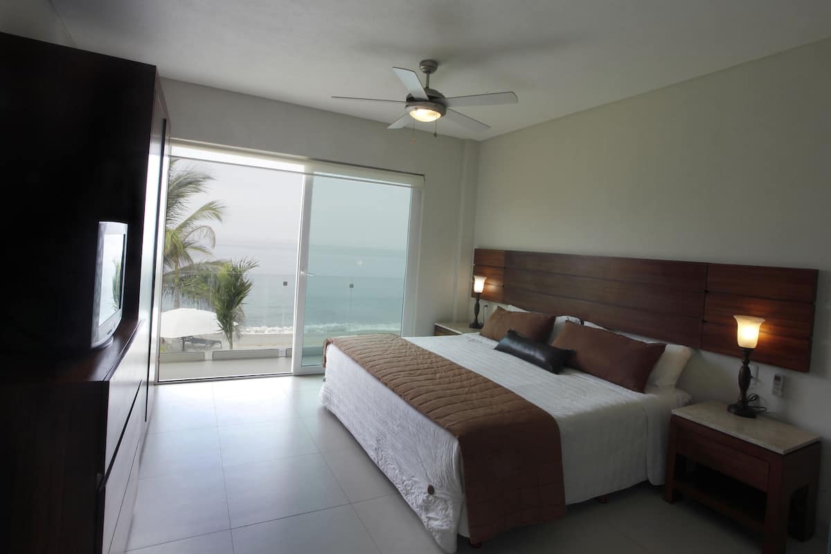 A bedroom with a bed, bedside tables, a ceiling fan, and a view of the ocean.