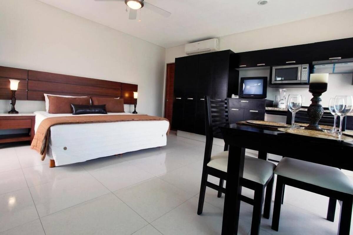 A hotel room with a bed, a desk, a chair, a television, and a kitchen area with a microwave.