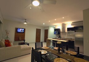 Una sala de estar moderna con un sofá, una mesa de comedor para cuatro personas y una zona de cocina con microondas y refrigerador.