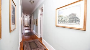 A hallway with framed pictures on the walls, wooden flooring, and a door at the end. - Esplanade Suites (New Orleans)