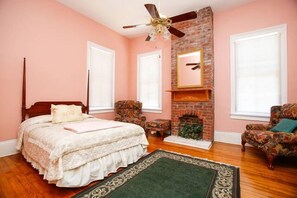 A bedroom with a bed, two chairs, a fireplace, and a ceiling fan. - Esplanade Suites (New Orleans)