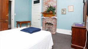 A bedroom with a bed, a brick fireplace, a wooden dresser, and a door. - Esplanade Suites (New Orleans)