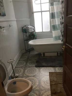 A bathroom with a toilet, a bathtub, and a window with a curtain. - Esplanade Suites (New Orleans)