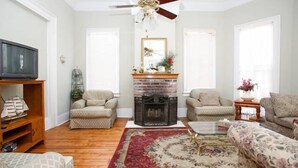 A living room with a fireplace, two armchairs, a sofa, a television, and a ceiling fan. - Esplanade Suites (New Orleans)