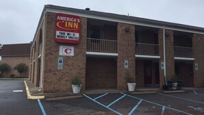 Un bâtiment à deux étages, sur lequel on peut voir une enseigne indiquant « America's Inn ». Il dispose d'un parking avec des places délimitées et des places de stationnement réservées aux personnes handicapées.