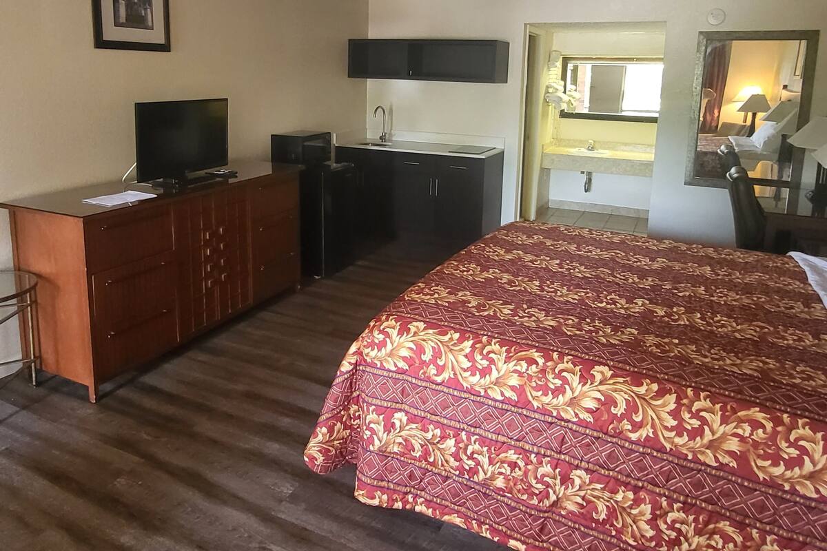 A hotel room with a bed, a desk, a television, a mirror, and a bathroom visible through an open door.