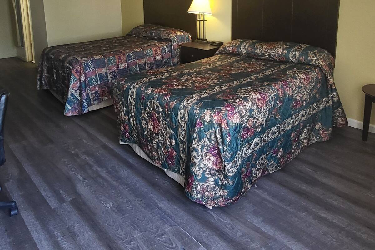 A hotel room with two beds, a nightstand with a lamp, and two framed pictures on the wall.