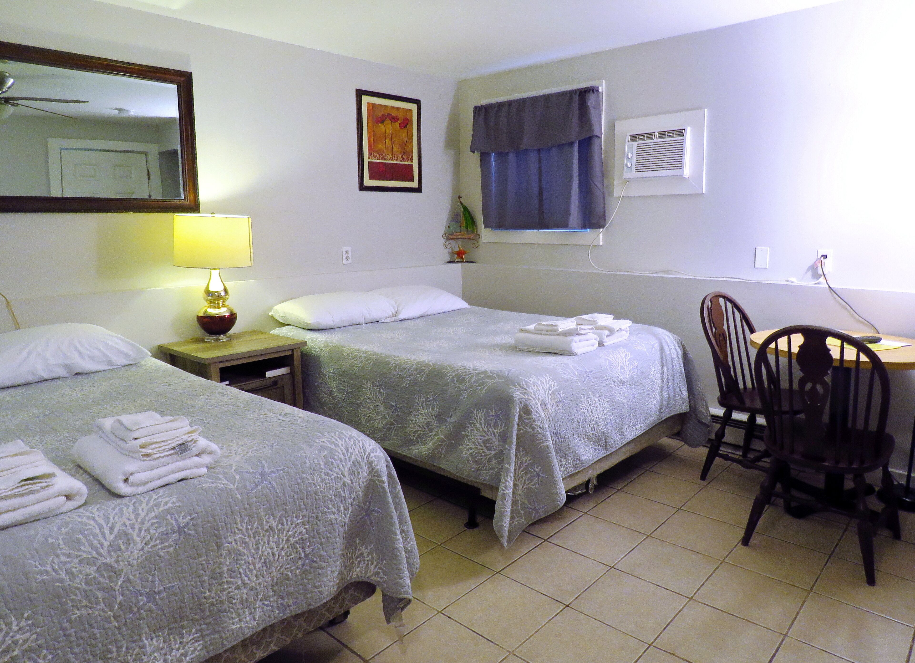 A hotel room with two beds, a desk, a chair, a lamp, and a window with curtains.