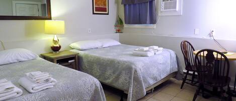 A hotel room with two beds, a desk, a chair, a lamp, and a window with curtains.