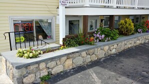 A building with a stone retaining wall, a porch, and a variety of flowers. - Breakers by the Sea (Hampton)