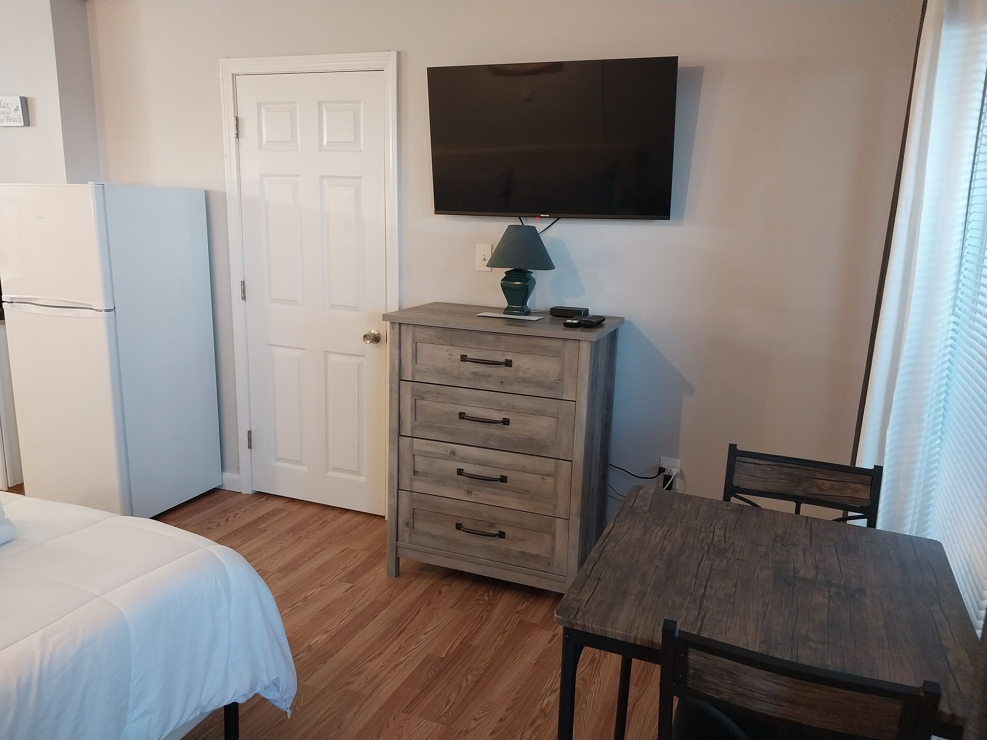 A bedroom with a bed, a dresser, a television, and a window with blinds.