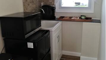 A compact kitchen with a microwave, stove, and small refrigerator. There's a window with curtains, a tiled backsplash, and a wooden countertop.