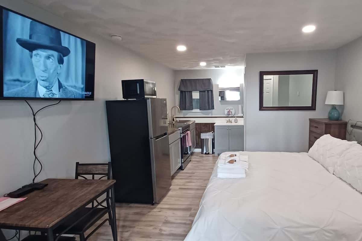 Ein Hotelzimmer mit Bett, Schreibtisch, Fernseher, einer Küchenzeile und einem Badezimmer.