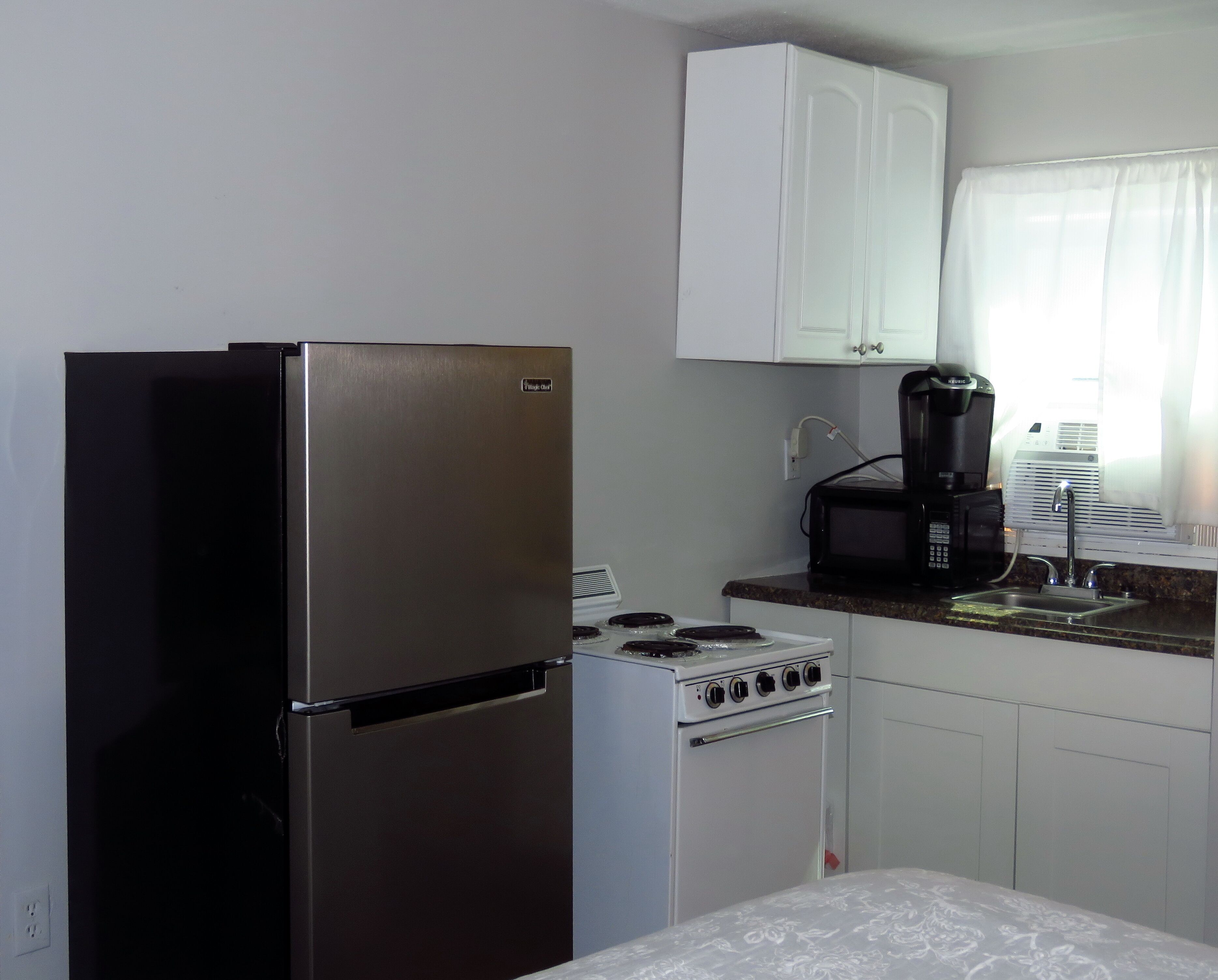 A compact kitchen with a stainless steel refrigerator, a white stove, and a coffee maker on the countertop.