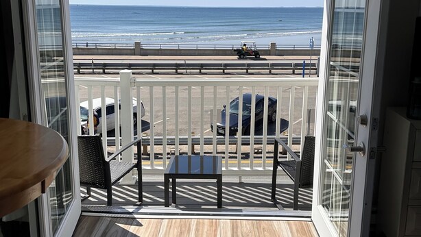 A balcony with a view of the beach, a table, and chairs. - Breakers by the Sea (Hampton)