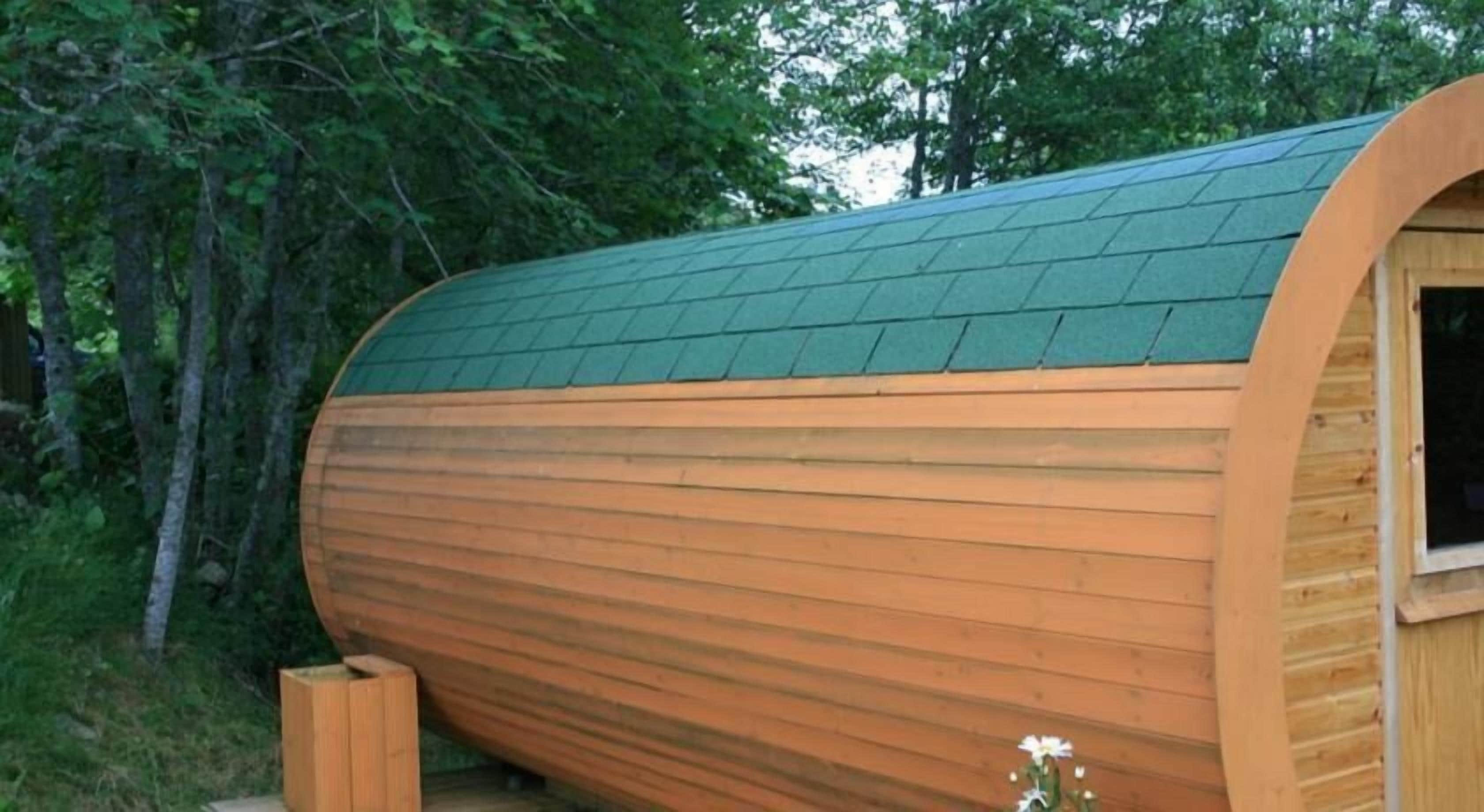 A wooden cylindrical structure with a green roof, surrounded by trees.