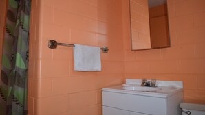 A bathroom with orange tiled walls, a white sink, a mirror, and a towel hanging on a metal towel rack. - Admiral Motel (Indianapolis)