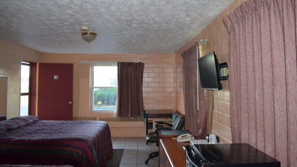 A hotel room with a bed, a desk with a telephone, a television, and a window with curtains. - Admiral Motel (Indianapolis)